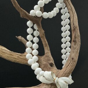 White Vendome bow necklace artistically hung on a driftwood branch with black background
