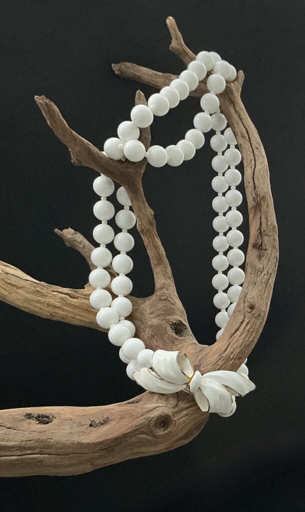 White Vendome bow necklace artistically hung on a driftwood branch with black background