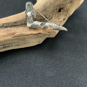 Mermaid brooch with coiled fishtail set upon a driftwood branch with black background