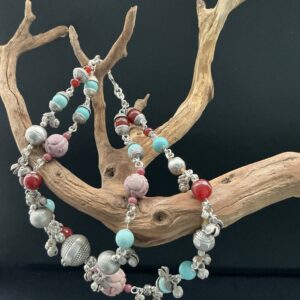 Tribal gemstone necklace with bells hanging on a driftwood branch on black background