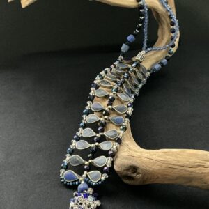 lapis ladder necklace draped over a driftwood branch with black background