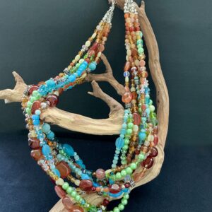 Multistrand gemstone necklace hanging on a driftwood branch with black background