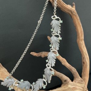 Silver Tone Thermoset Grey Leaf Necklace hanging on a dritwood branch with black background