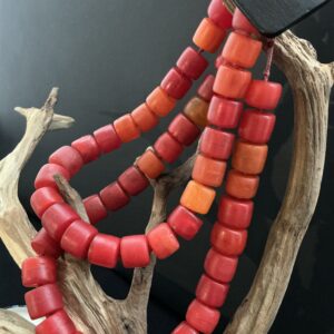 deep red-orange colored venitian trade bead necklace artistically draped over a driftwood branch with black background