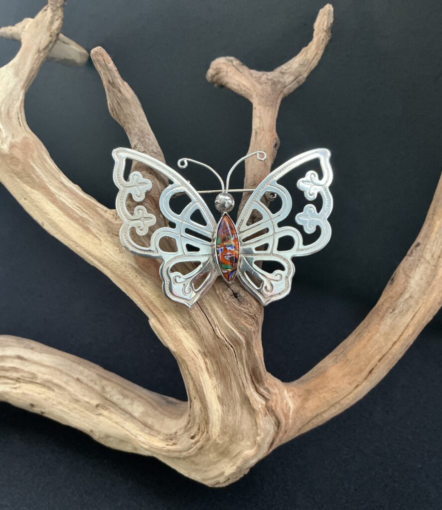 silver butterfly brooch hung on a piece of driftwood with black background