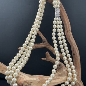 JBK white triple strand faux pearl necklace draped over a driftwood branch with black background.