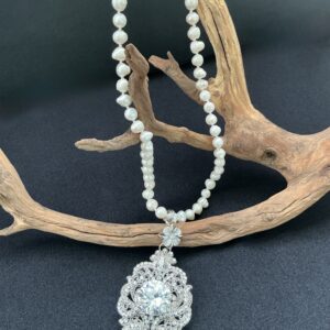 White FWP necklace with large silver tone filigree clear rhinestone pendant draped over driftwood branch with blackbackground