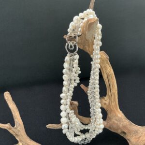 White FWP with clear crystal multistrand necklace hanging on a driftwood branch with black background