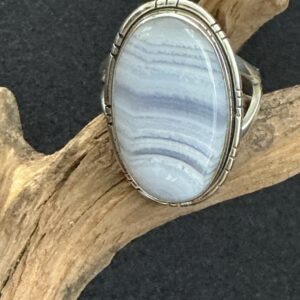 Blue lace agate oval statement ring seated upon a driftwood branch with balce background