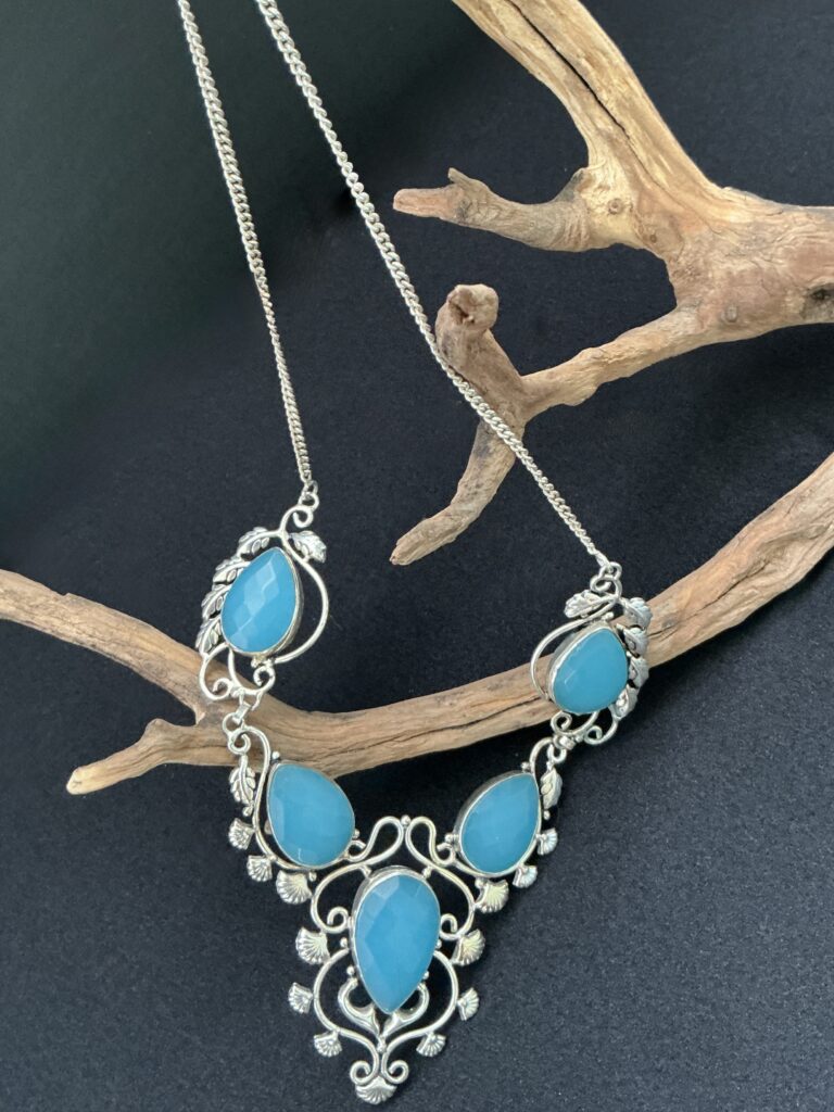 Artisan sterling blue chalcedony statement necklace draped on a driftwood branch with black background