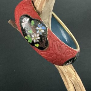 Cinnabar cloisonne bangle hanging in a driftwood branch with black background