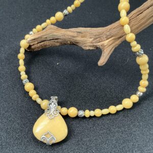 Yellow jasper pendant necklace draped over a driftwood branch on a black background