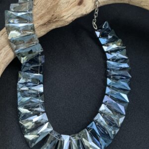 Smokey glass segmented choker necklace draped over a driftwood branch with a black background
