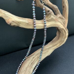 Peacock pearl necklace hanging on a branch of driftwood with a black background