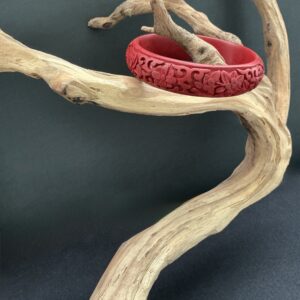 Cared red cinnabar bangle hung from a driftwood branch on a black background