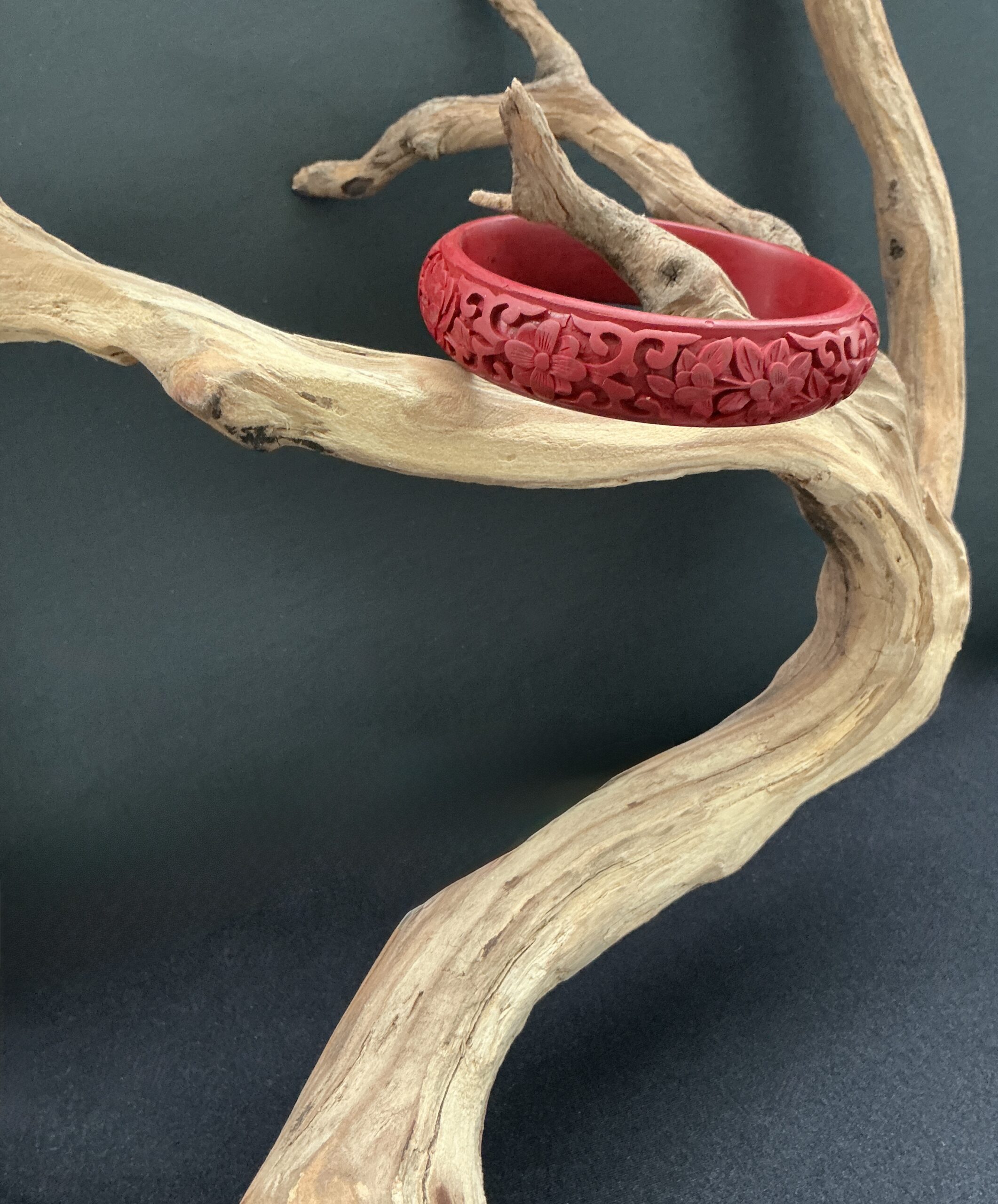 Cared red cinnabar bangle hung from a driftwood branch on a black background