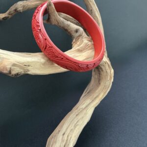 Red carved cinnabar bangle hung on a driftwood branch with black background