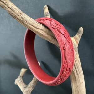 Red cinnabar bangle hanging on a driftwood brand with a black background