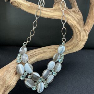Blue lace agate and topaz bib necklace hanging over a driftwood branch on black background