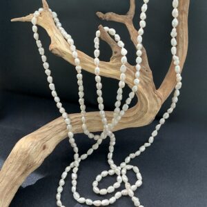 Very long white freshwater pearl necklace draped on a driftwood branch with a black background