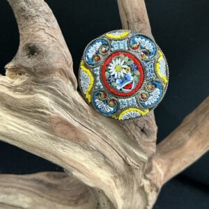 Micro mosaic colorful round vintage pin perched on a driftwood branch with black background
