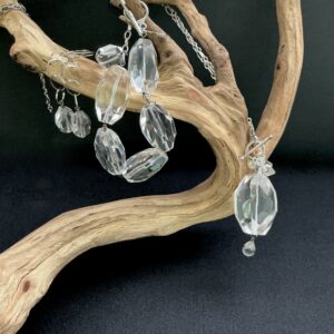 Rock crystal jewelry set hanging on adriftwood branch with a black background