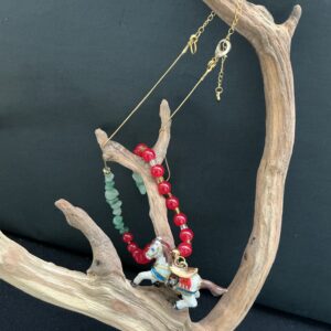 Horse pendant charm with gemstones on a gold tone snake chaing hanging on a driftwood branch with a black background