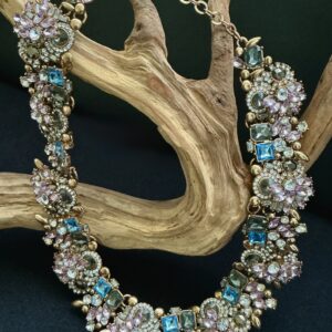 Gold tone Pastel rhinestone encrusted collar necklace hanging on a bramch of driftwood with a black background