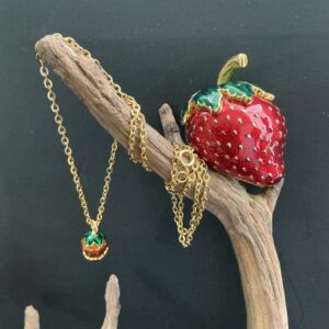 Edgar berebi strawberry box and small pendant necklace perched and hanging on a branch with a black background