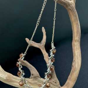 Brown thermoset bar link necklace hung on a branch with a black background