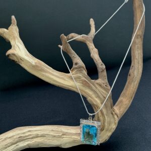 Faceted Blue topaz art glass silver tone pendant necklace hung on a branch with black background