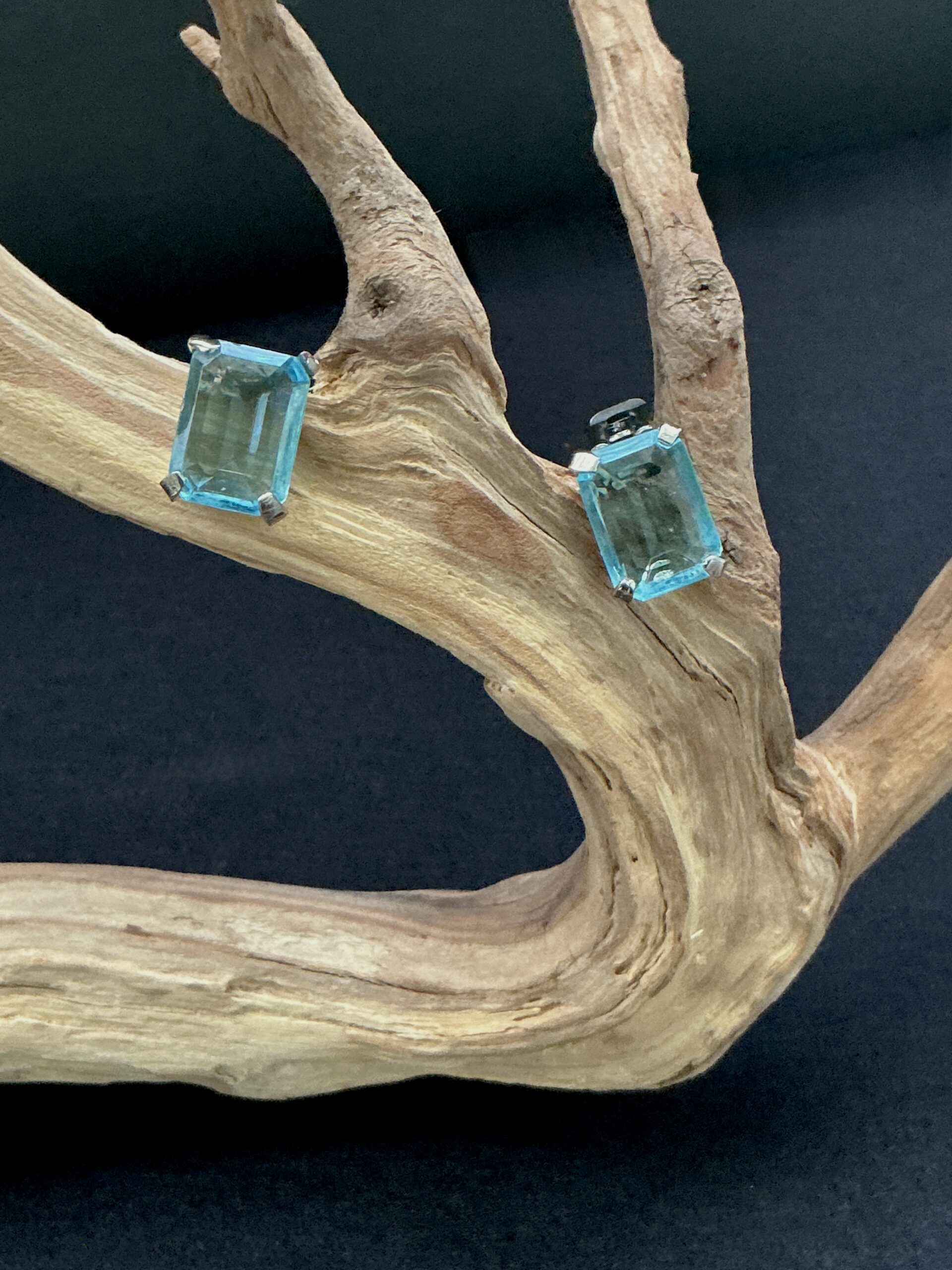 Pair of Blue topaz faceted art glass clip on earrings perched on a branch with a black background