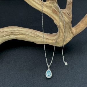 Blue topaz sterling silver pendant necklace hung on a branch with a black background