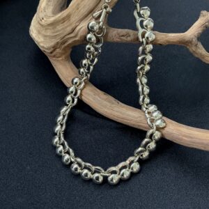 Signed Monet silver tone choker necklace with polished bead links and curved modernist design displayed on natural wood branch.