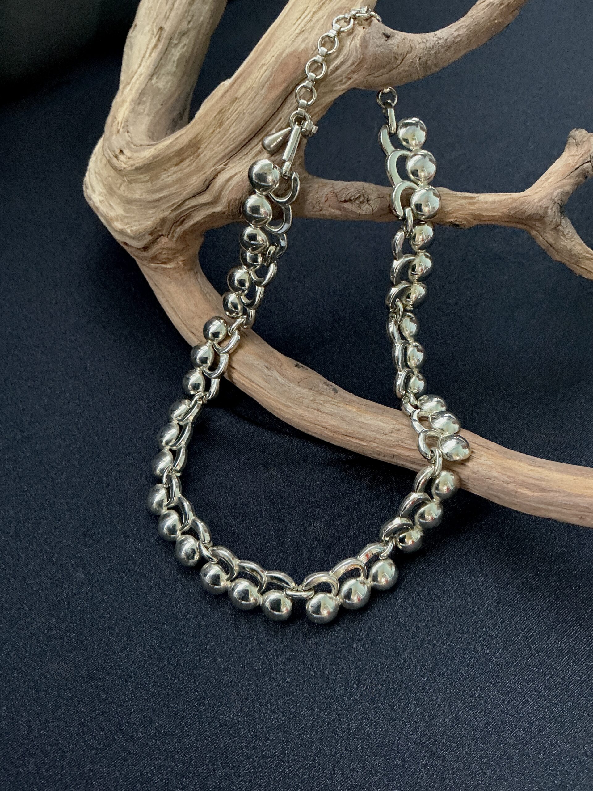 Signed Monet silver tone choker necklace with polished bead links and curved modernist design displayed on natural wood branch.