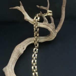 Gold Tone Geometric design choker necklace draped on a branch with black background