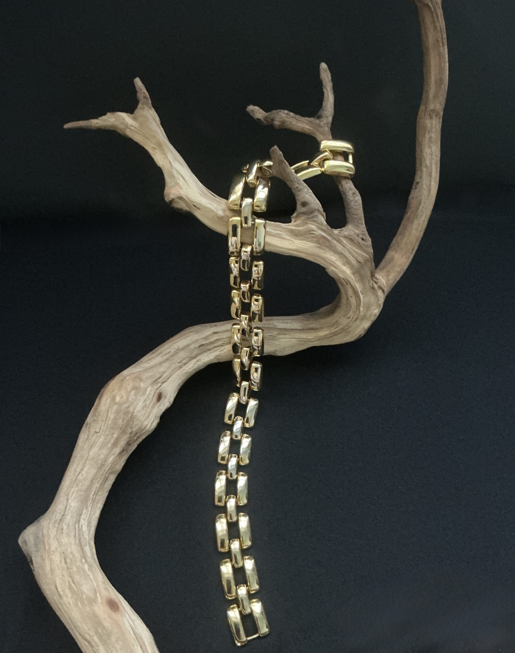 Gold Tone Geometric design choker necklace draped on a branch with black background