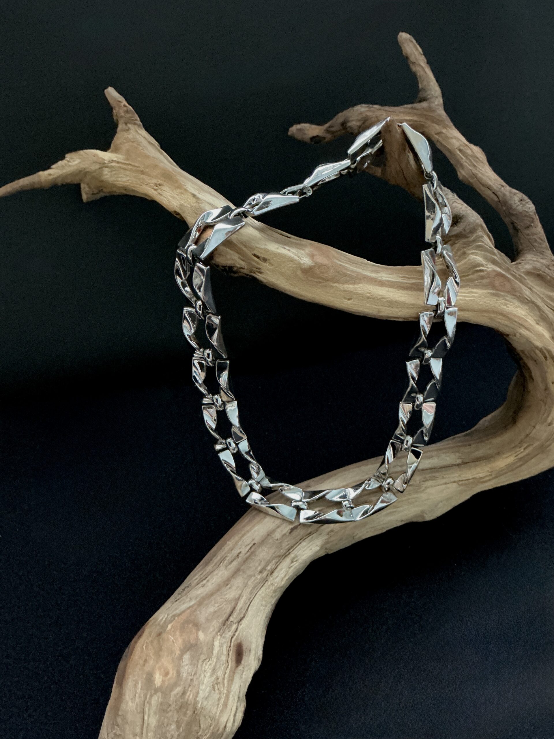 Silver square twist open link choker necklace draped over a branch with a black background