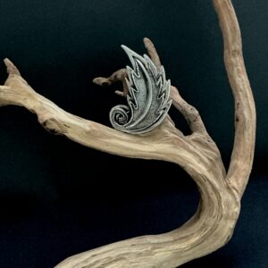 Silvertone Tortolani leaf brooch perched on a branch with black background