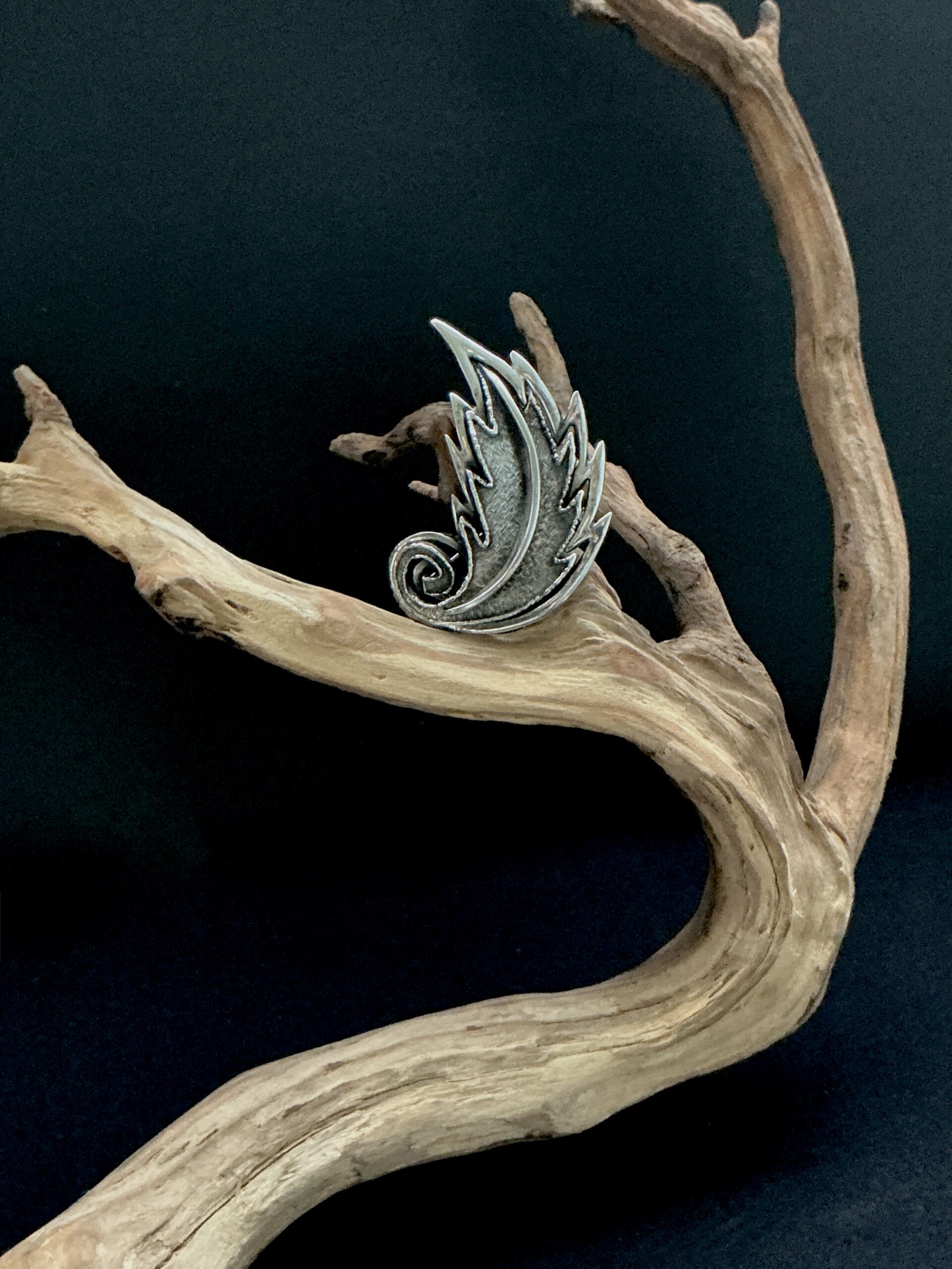 Silvertone Tortolani leaf brooch perched on a branch with black background
