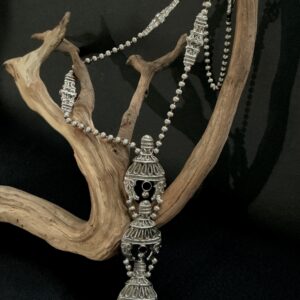 vintage KJL silver tone long pendant necklace draped over a branch with black background
