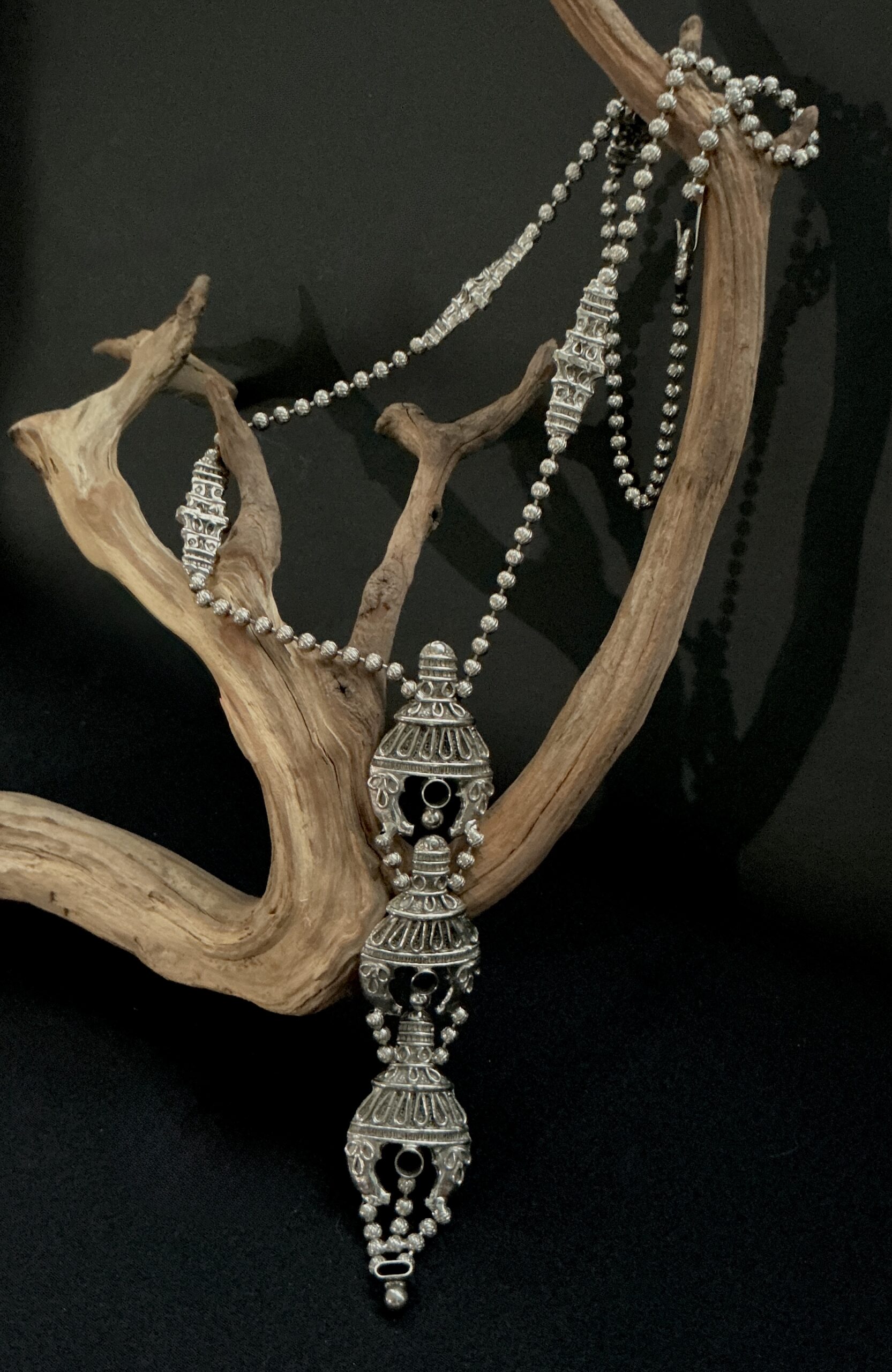 vintage KJL silver tone long pendant necklace draped over a branch with black background