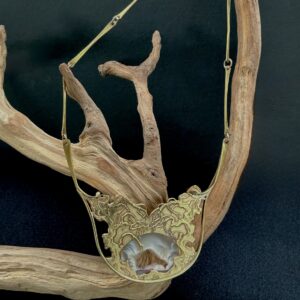 Brass Artisan necklace with druzt agate pendant draped over a branch with black background