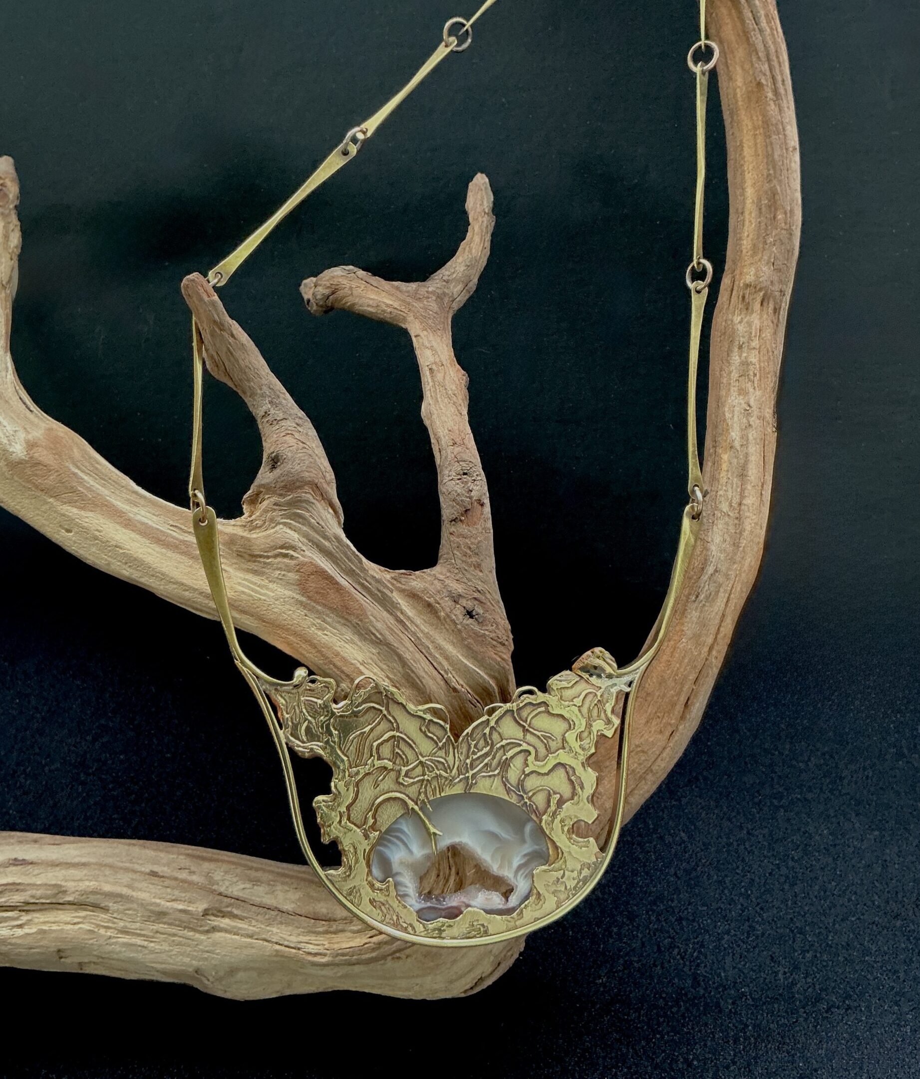 Brass Artisan necklace with druzt agate pendant draped over a branch with black background