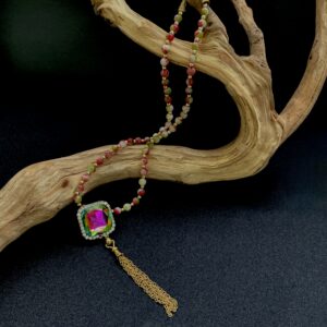 Colorful pendant and stone bead necklace draped over a branch with black background