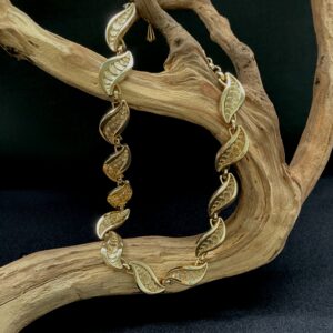 Scalloped gold tone necklace draped on a branch with black background