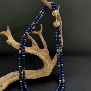 Blue KJL double strand necklace with Rams head clasp draped over a branch with black background