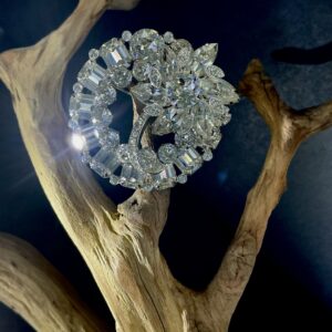Round silver tone eisenberg clear rhinestone brooch perched on a branch with black background