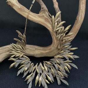Long brass leaf with clear rhinestones statement bib necklace draped on a branch with black background