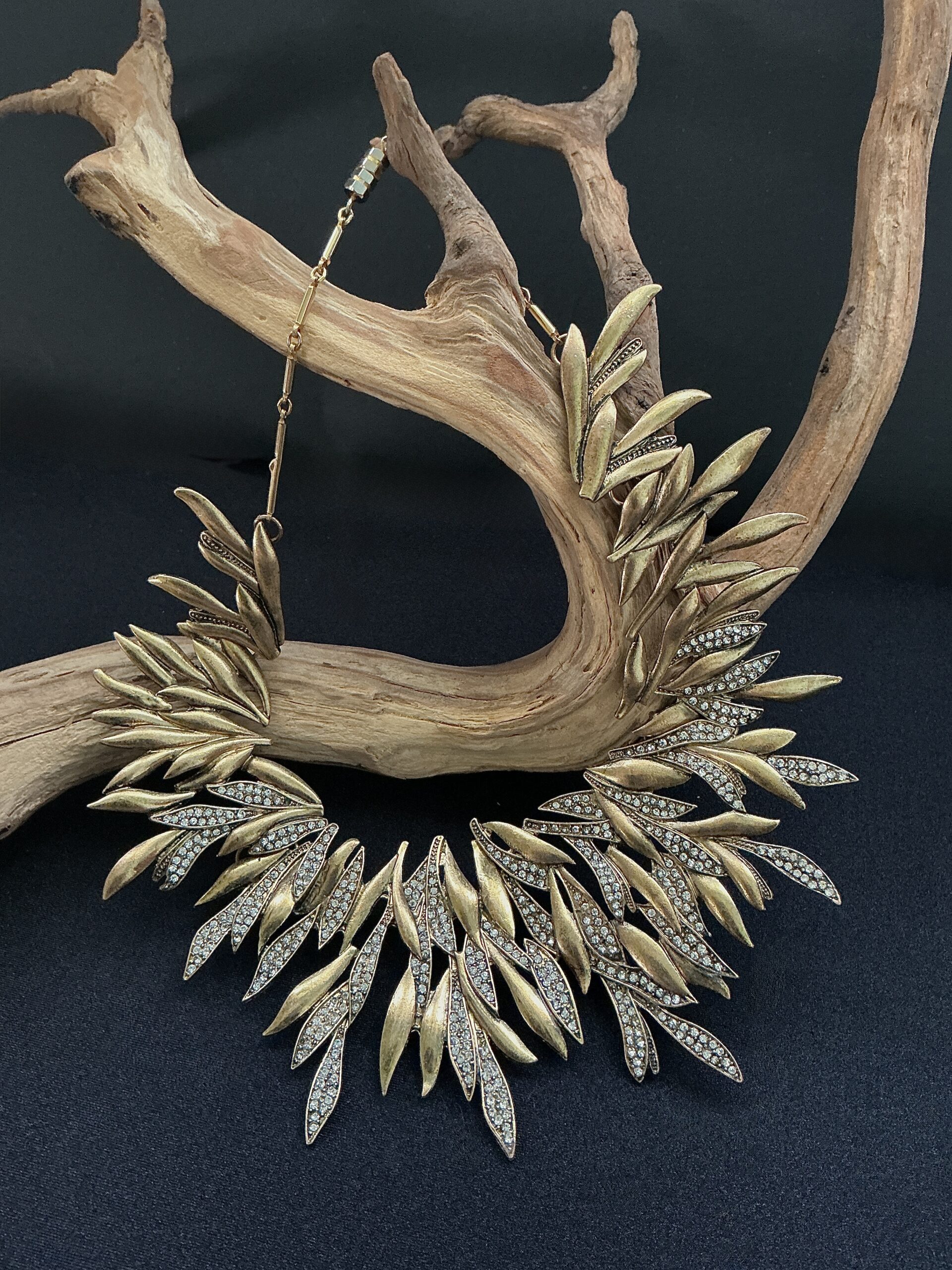 Long brass leaf with clear rhinestones statement bib necklace draped on a branch with black background